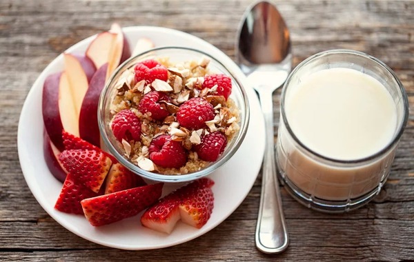 Desayuno sencillo con frutas, avena y un vaso de agua sobre mesa clara